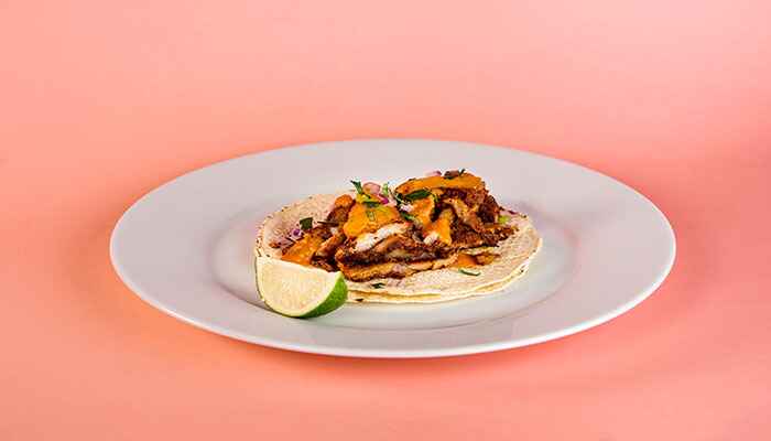 A taco with
      orange vegetables on a plate with an orange background color