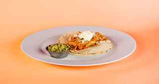 A taco with
        side of guacamole on a white plate on an orange background.