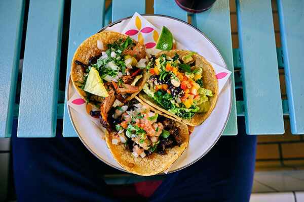 Three street tacos sitting on a light blue wooden table